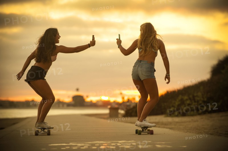 Teenage girls riding skateboards holding cell phones