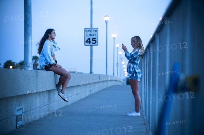 Teenage girl photographing friend sitting on wall