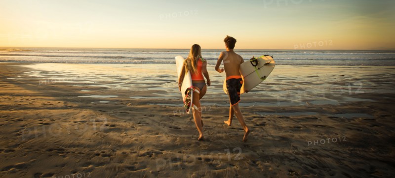 Teenage boy and girl carrying surfboards running to ocean