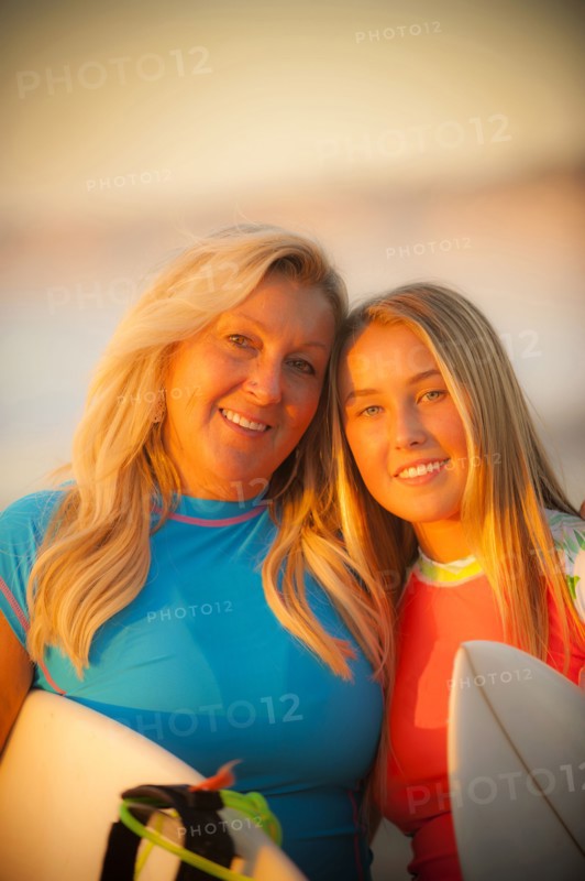Portrait of smiling Caucasian mother and daughter holding surfboards