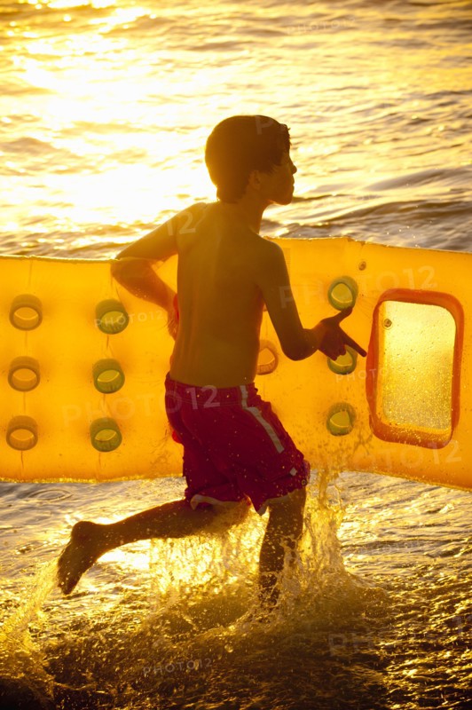 Caucasian boy running into ocean carrying inflatable raft