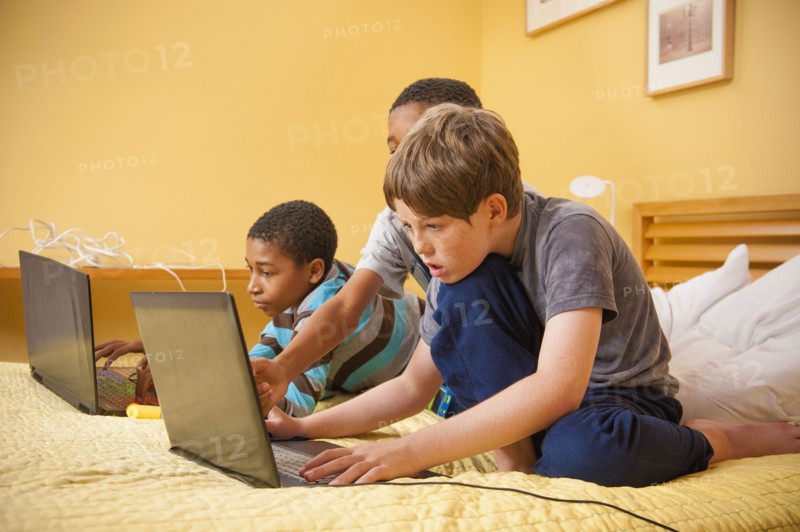 Boys sitting on bed using laptops