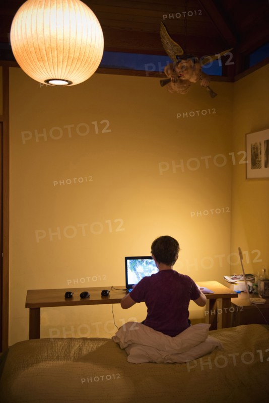 Caucasian boy sitting on bed using laptop