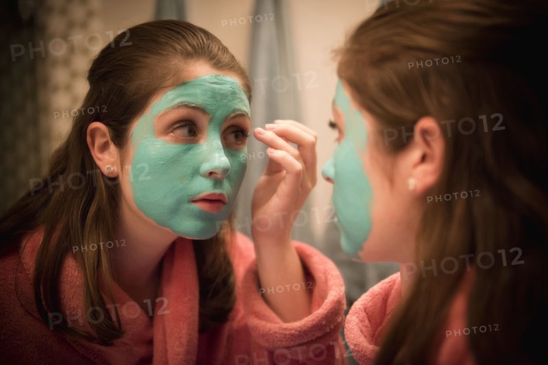 Caucasian girl applying facial mask in mirror