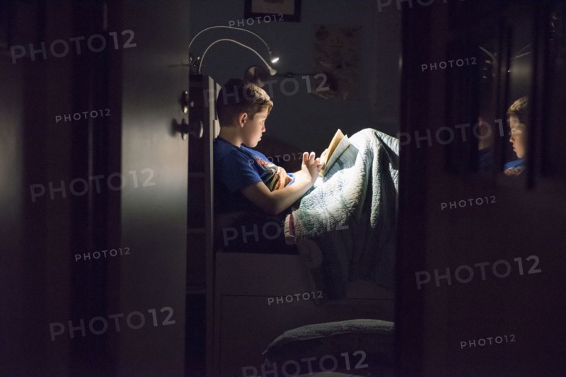Caucasian boy reading book in bed at night