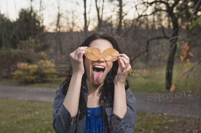 Playful Caucasian woman with leaves covering her eyes