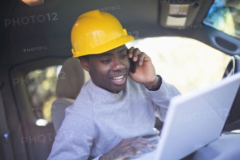 Black man wearing hard hat in vehicle using laptop