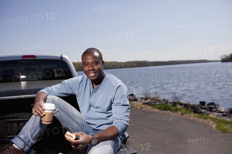 Black man sitting in truck bed eating lunch