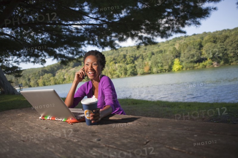 African American businesswoman sitting at picnic bench talking on cell phone