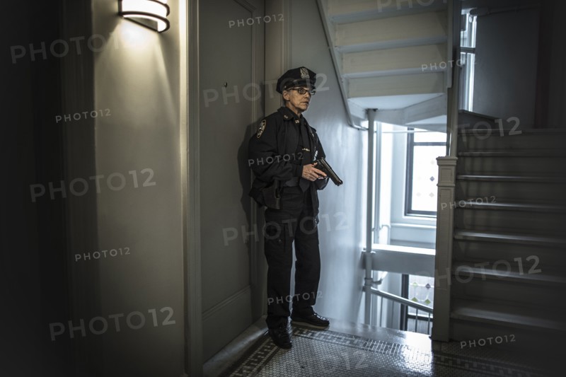 Older Caucasian policewoman holding gun in apartment staircase