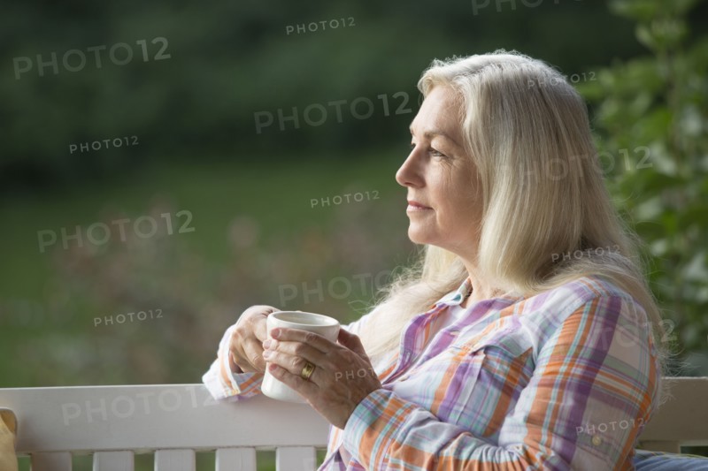Older Caucasian woman drinking cup of coffee on porch swing