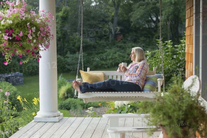 Older Caucasian woman drinking cup of coffee on porch swing