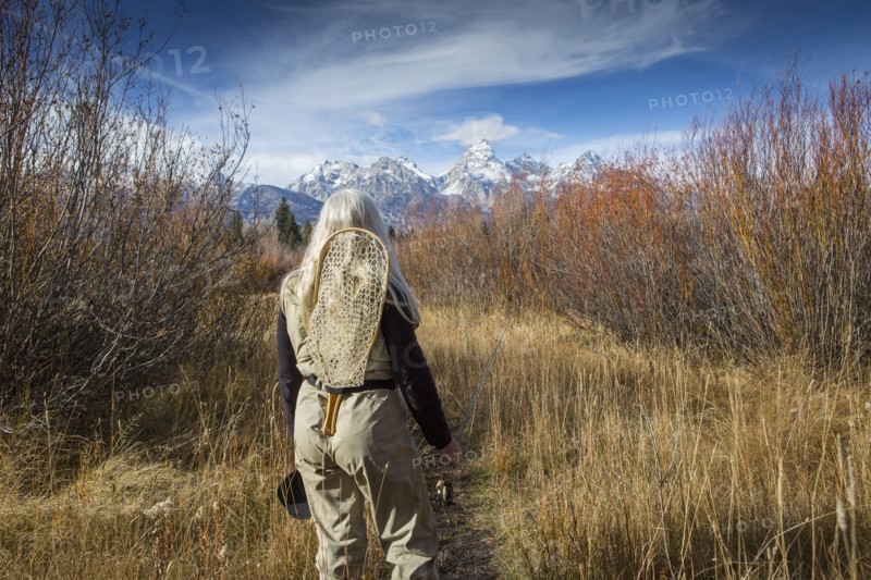 Older Caucasian woman carrying fishing supplies in field