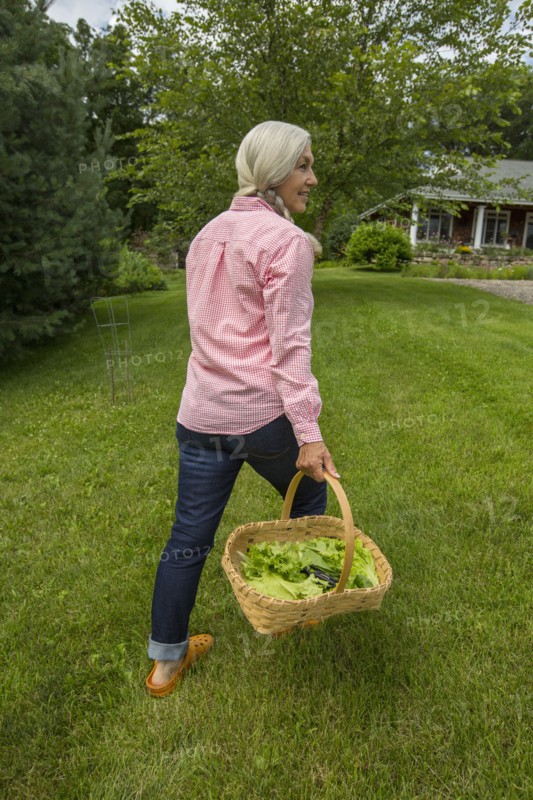 Caucasian woman carrying basket of vegetables in backyard
