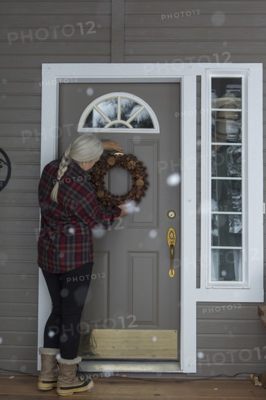 Older Caucasian woman hanging wreath on front door