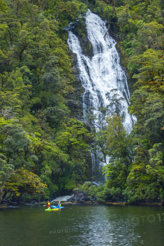 Caucasian friends paddling kayak under remote waterfall
