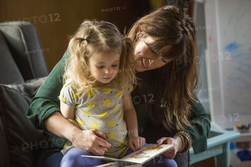 Caucasian mother and daughter reading book on sofa