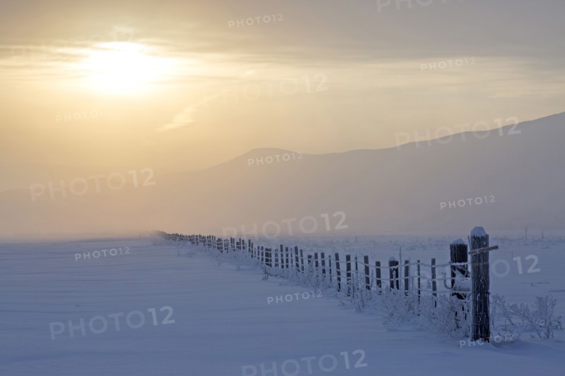 Sunrise over fence in snowy rural landscape