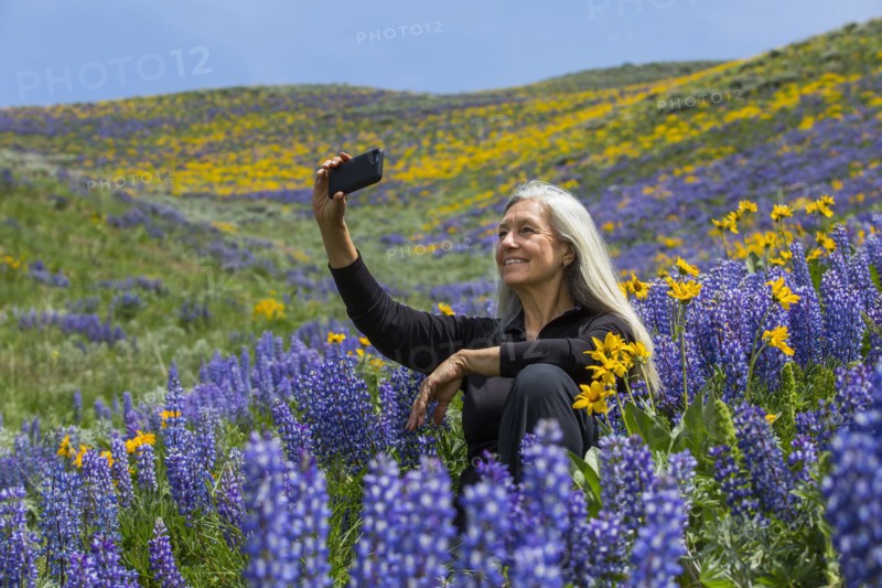 Caucasian woman posing for cell phone selfie hillside with wildflowers