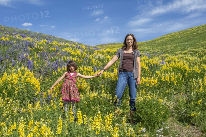 Caucasian mother and daughter standing on hillside with wildflowers