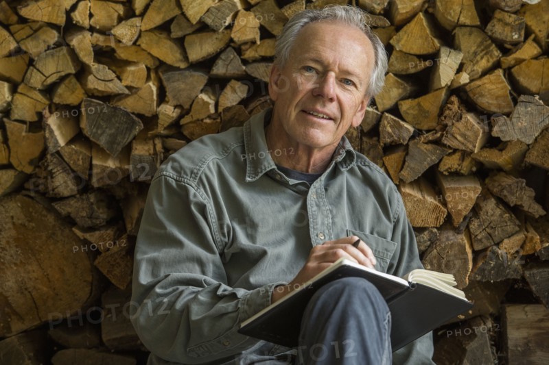 Caucasian man leaning on woodpile writing in journal