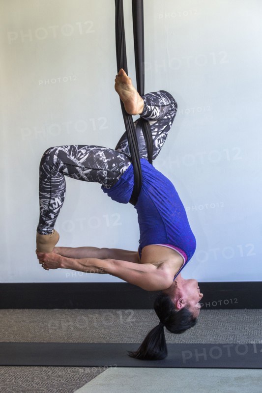 Mixed race woman performing yoga hanging from silks