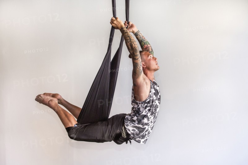 Mixed Race man performing yoga hanging from silks