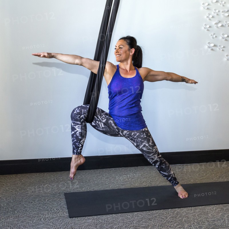 Mixed Race woman performing yoga hanging from silks