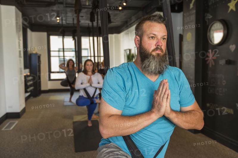 Caucasian man meditating hanging from silks