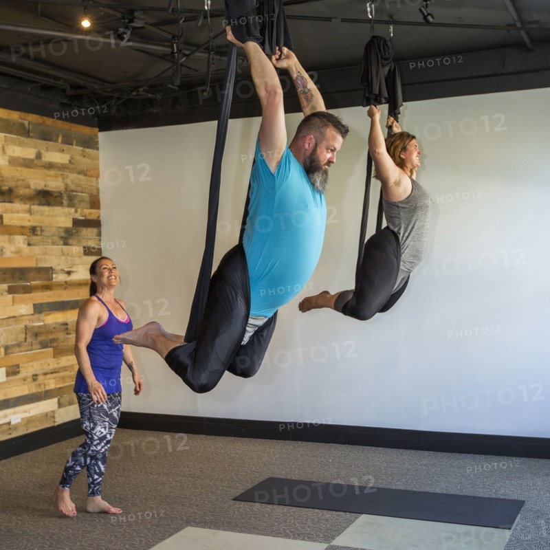 Instructor watching students performing yoga hanging from silks
