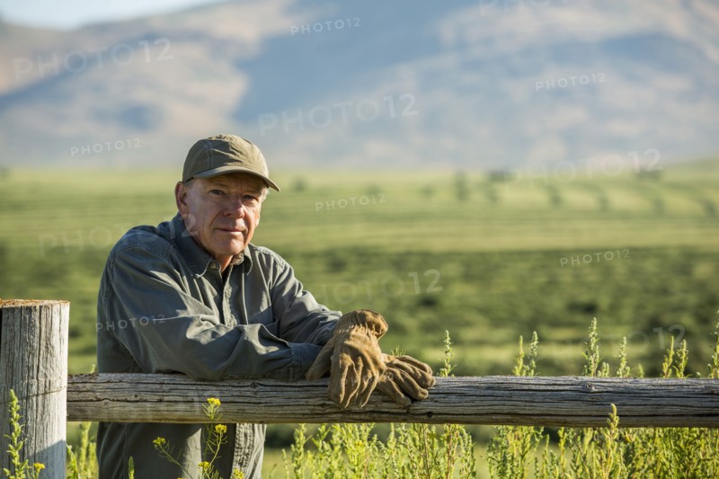 Caucasian farmer wearing gloves leaning on wooden fence