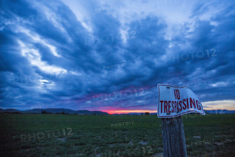No trespassing sign under clouds at sunset