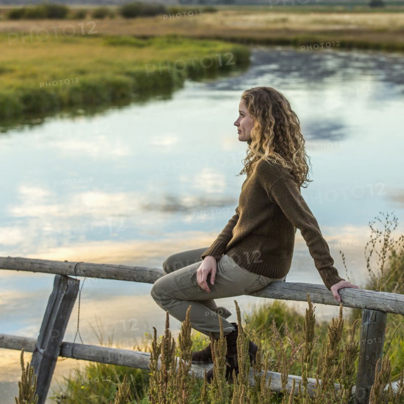 Caucasian woman sitting on wooden fence near river