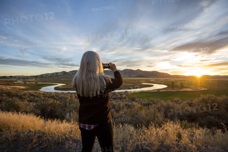 Caucasian woman photographing sunset over winding river