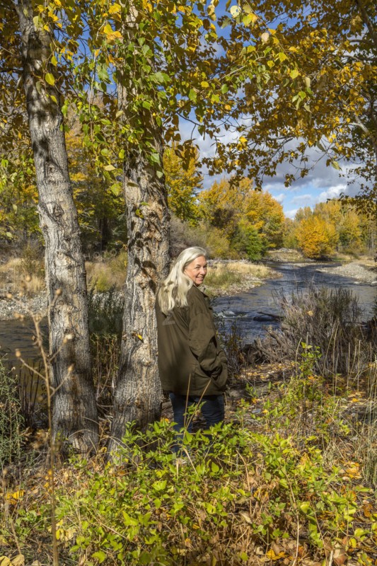 Smiling Caucasian woman leaning on tree near river