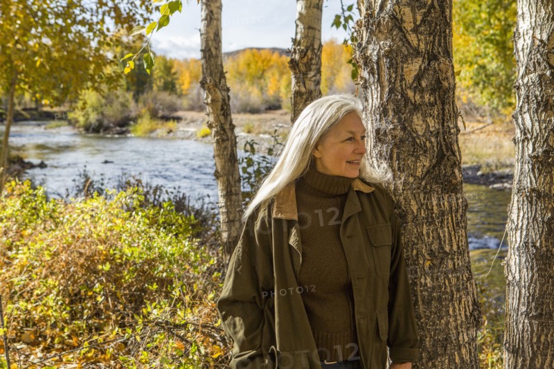 Smiling Caucasian woman leaning on tree near river