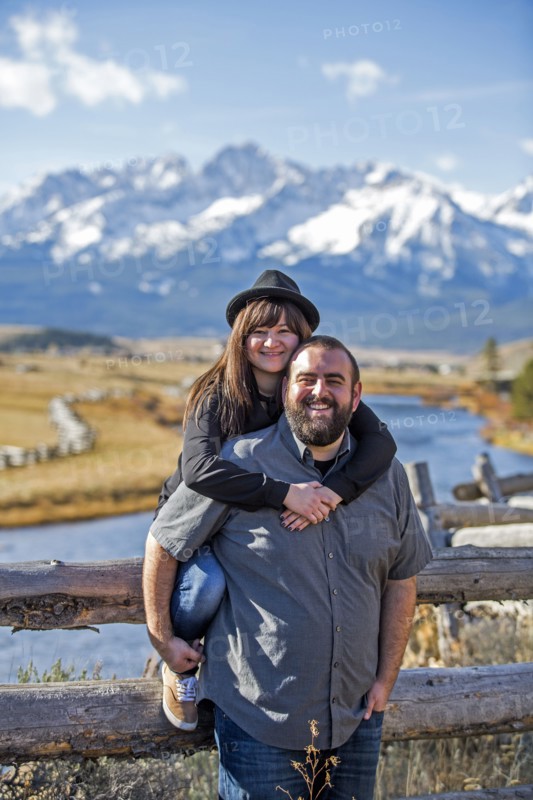 Smiling Caucasian couple posing at wooden fence near river