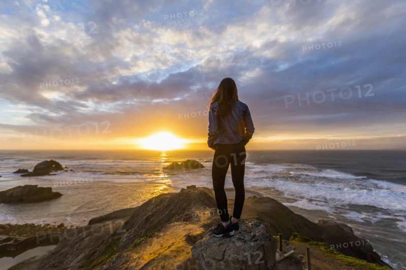 Caucasian woman standing on rock near ocean at sunset