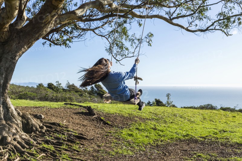 Caucasian woman on tree swing near ocean
