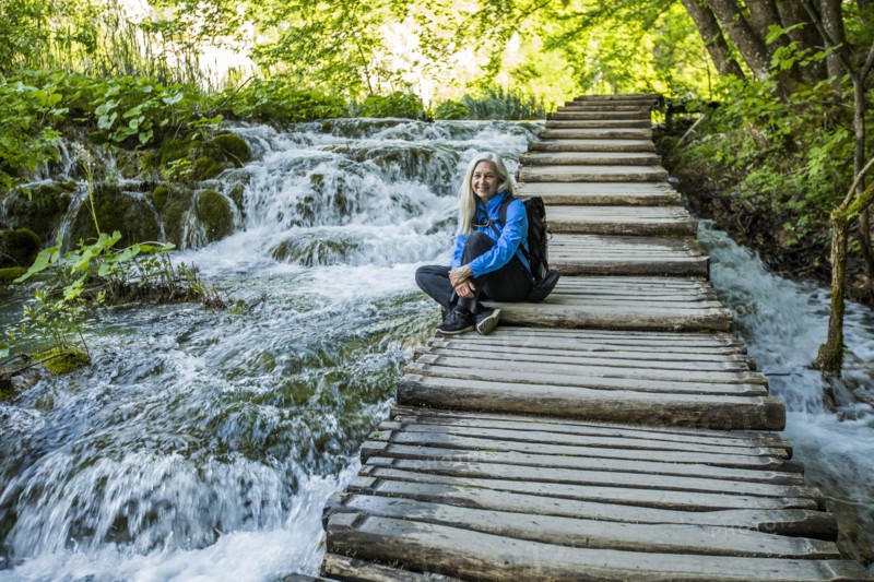 Older Caucasian woman sitting on wooden staircase over waterfalls