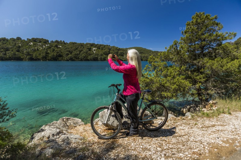 Caucasian woman on bicycle photographing lake with cell phone