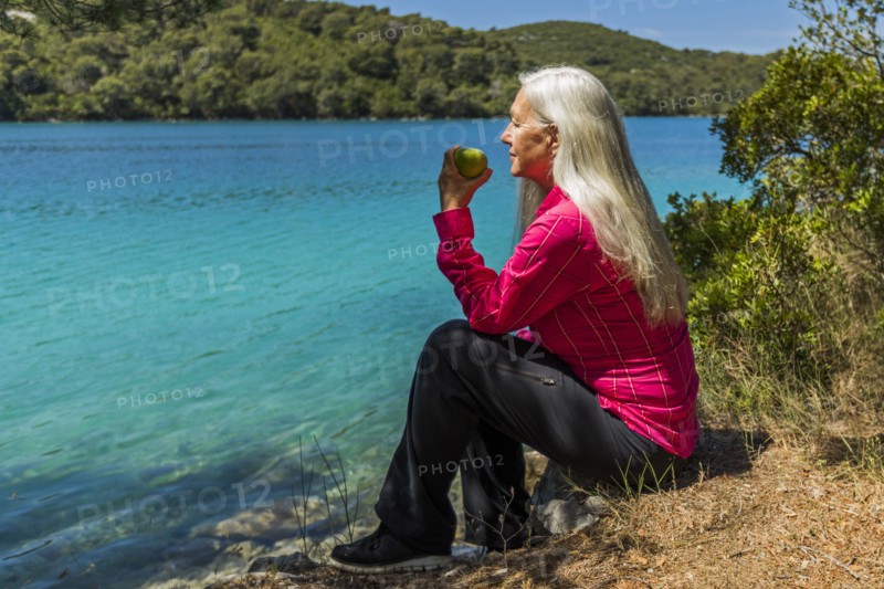 Caucasian woman sitting at lake eating apple