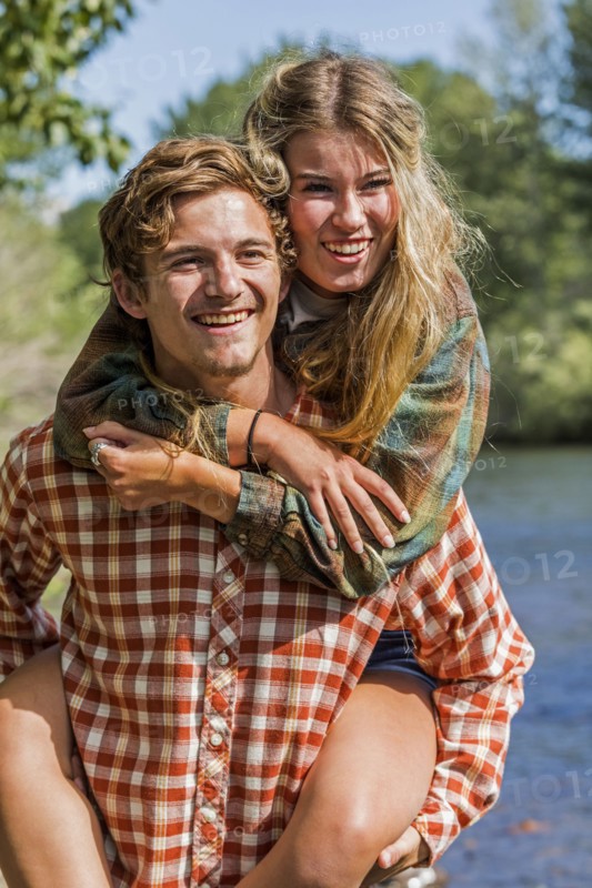 Caucasian boy carrying girl piggyback at river