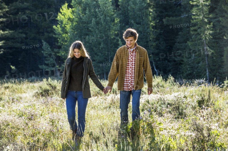 Caucasian couple walking in field holding hands