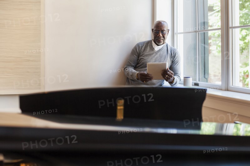 Man using digital tablet near window behind piano