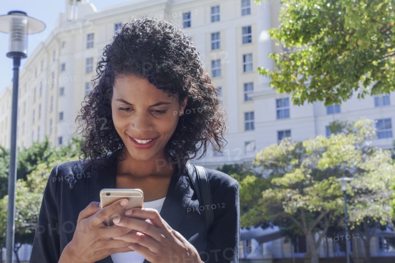 Mixed Race businesswoman texting on cell phone outdoors