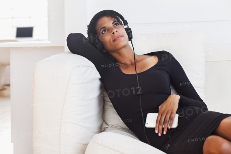 Mixed Race woman on sofa listening to cell phone with headphones