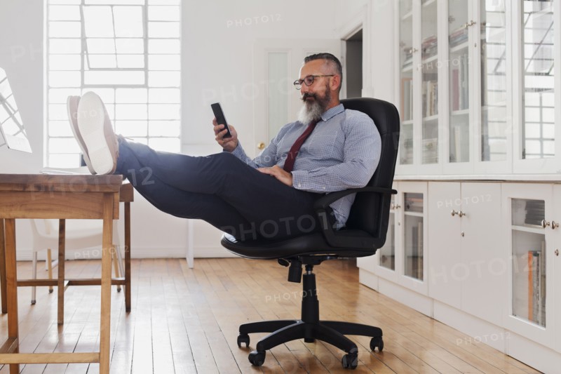 Caucasian man with feet up texting on cell phone
