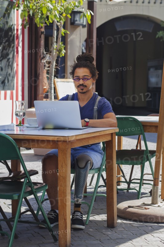 Mixed race man with prosthetic leg using laptop at sidewalk cafe