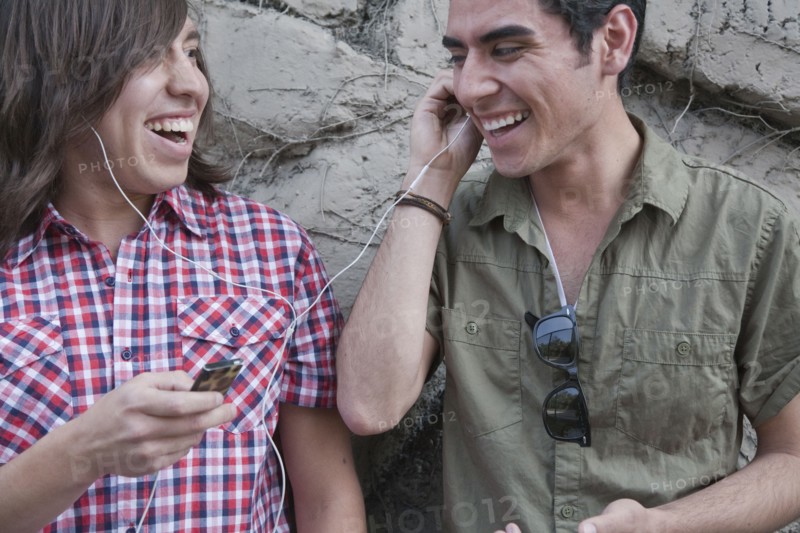 Smiling teenage boys sharing headphones and holding mp3 player
